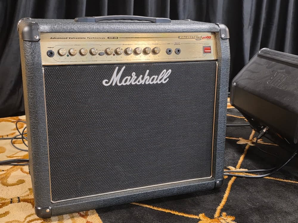 A Marshall combo amplifier on a patterned rug, its control panel gold above a black speaker grille.